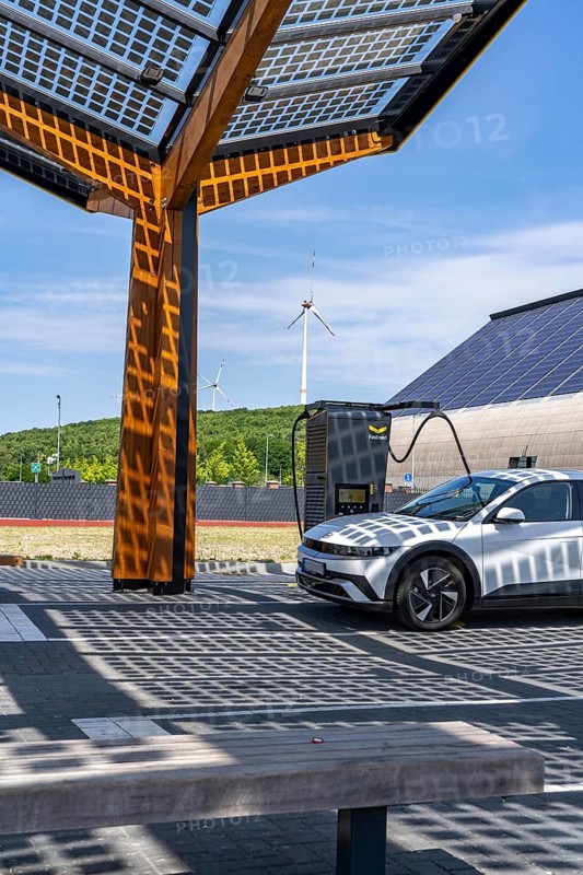 Electric charging station on the site of the former Lohberg colliery in Dinslaken, operated by Fastned, uses electricity from wind power and solar energy, fast-charging columns, with its own solar roof, in the background the 11, 500 square metre solar roof on the colliery's former coal mixing hall, wind farm on the Lohberg slagheap, North Rhine-Westphalia, Germany