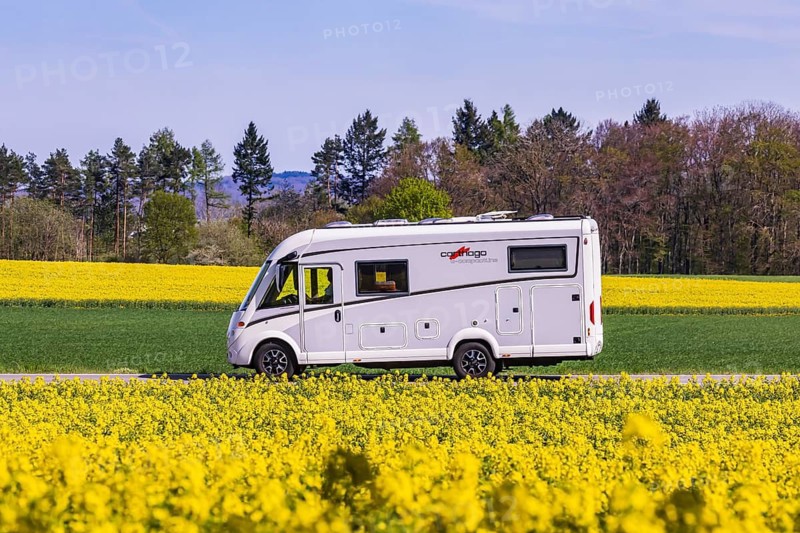 Country road with motorhome on the Swabian Alb with rape field in bloom. Erkenbrechtsweiler, Baden-Württemberg, Germany