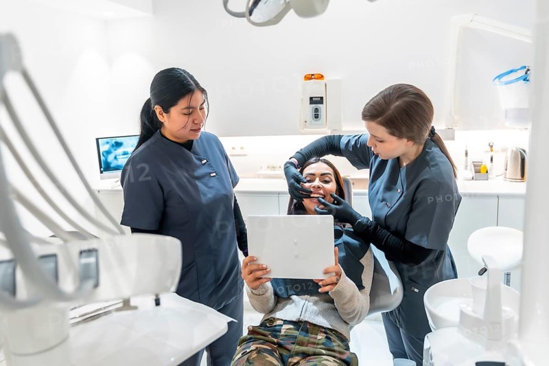 Female dentist showing teeth whitening results to happy patient holding a mirror in a modern dental clinic