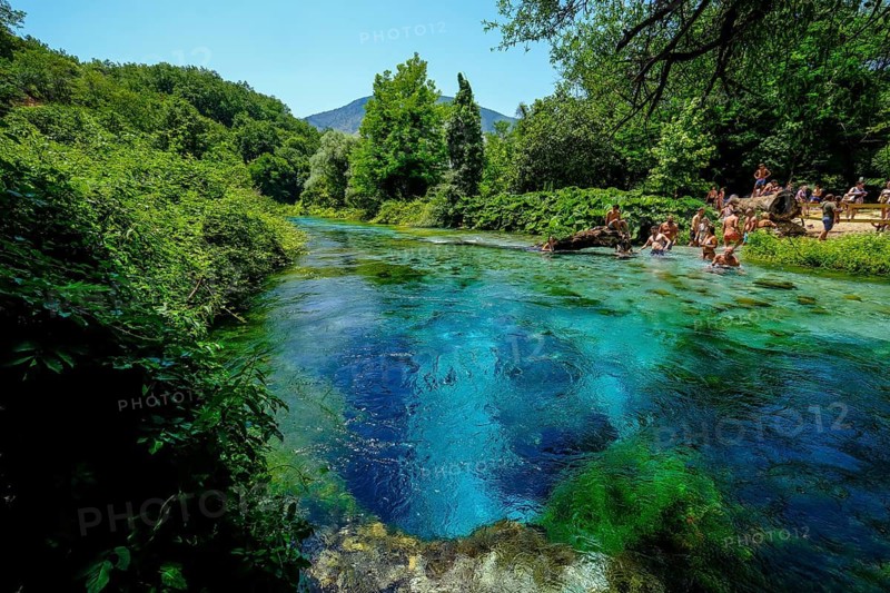 Muzina, Albania, tourists bathe in the Syri i Kaltër, THE BLUE EYE, is the country's most water-rich spring at 6 metres per second. The water emerges from a spring pot at a depth of more than 50 metres under high pressure. The water temperature is a fairly constant 12.75°C. The Blue Eye is located midway between the larger towns of Saranda on the coast and Gjirokastra inland