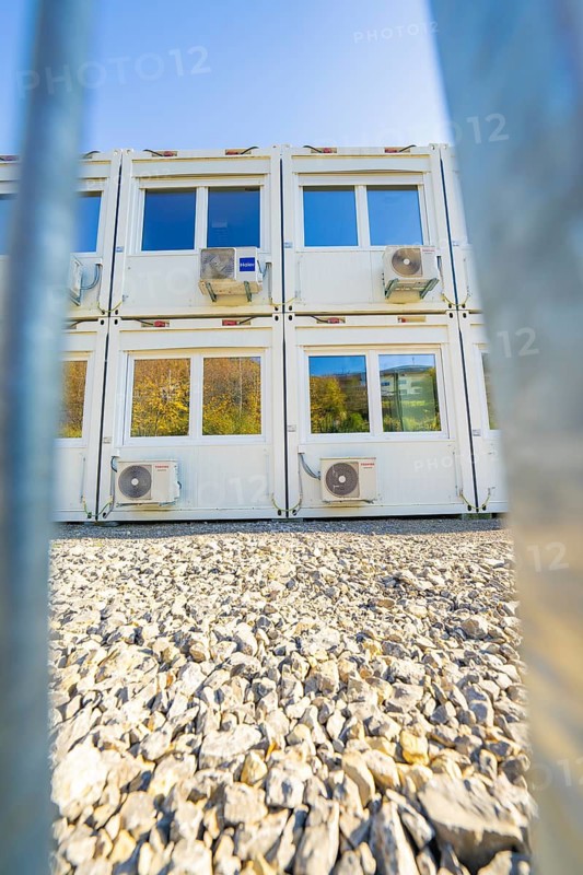 White containers with air conditioners on gravel surface, seen through a barrier system, in natural surroundings, refugee accommodation Beermiß, Calmbach, Black Forest, Germany