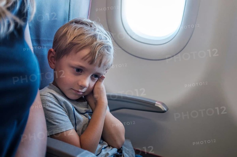 Boy in the airplane is holding his aching ear