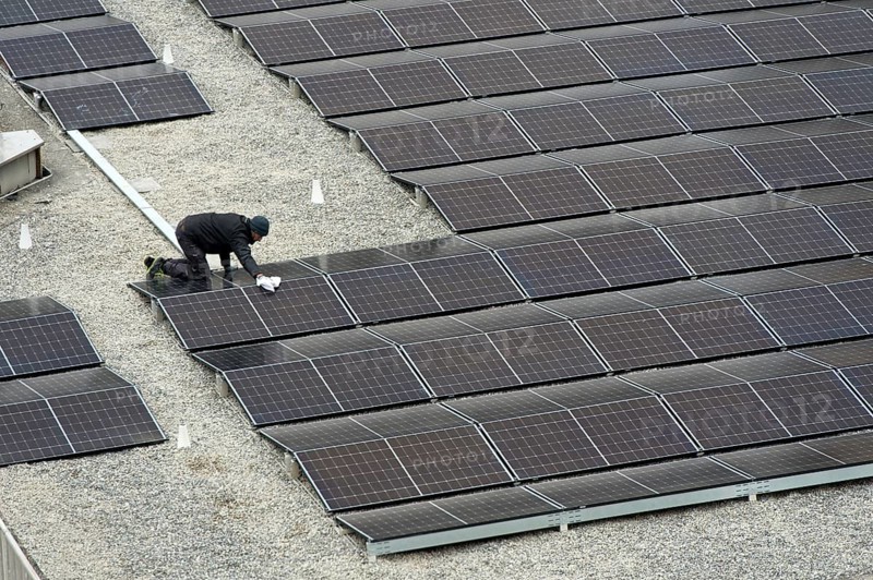 Technician cleans solar panels on the flat roof of the Varembé indoor swimming pool, Piscine de Varembé, in a mixed urban residential and office development, Geneva, Switzerland