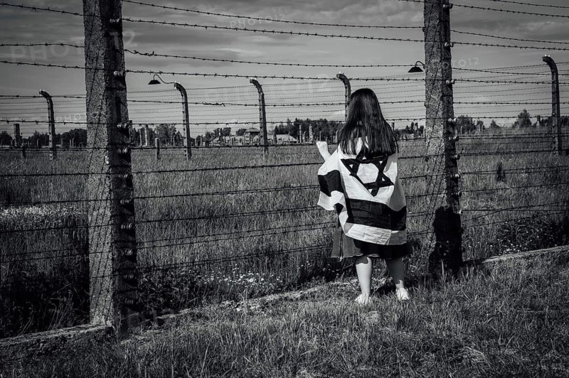Jewish girl with Israeli flag by the fence of the concentration camp