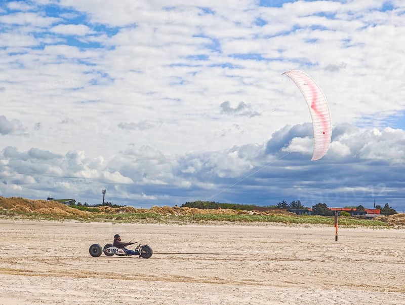 Recreational sport Beach kiting on the edge of the national park and UNESCO World Heritage Site, designated kite area, kite buggy steered with both feet, driver's seat with kiter between rear axle and front wheel, high speed, westerly winds, dunes on the beach, sunshine and blue sky, Sankt Peter-Ording, Schleswig-Holstein, Germany