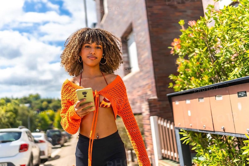 Brunette beauty woman using phone in the street walking along a residential area