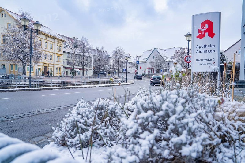 Snow-covered town street with pharmacy sign and surrounding buildings, Aidlingen, Böblingen district, Germany