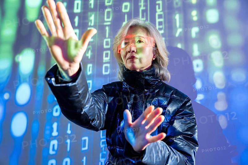 An elderly Asian woman interacts with virtual elements in the metaverse, wearing futuristic glasses and gesturing with her hands, surrounded by digital binary code