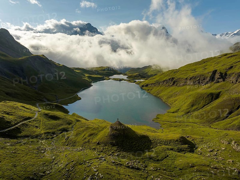 A breathtaking view of the serene Bachalpsee in Switzerland, surrounded by lush green hills and distant alpine mountains, under a sky blanketed with clouds