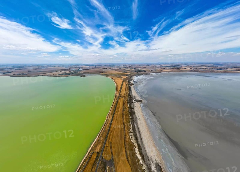 Aerial photo contrasting vibrant green and gray lakes divided by road in Victoria, Australia. Cloudy sky adds depth to this landscape, highlighting nature beauty