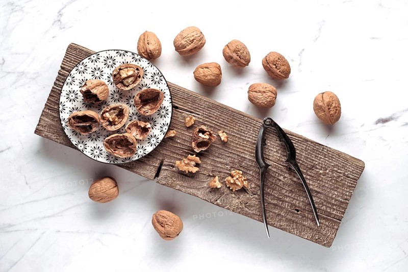 A rustic setup features whole and cracked walnuts on a patterned plate, with a nutcracker beside them, all displayed on a wooden board. A simple, natural scene