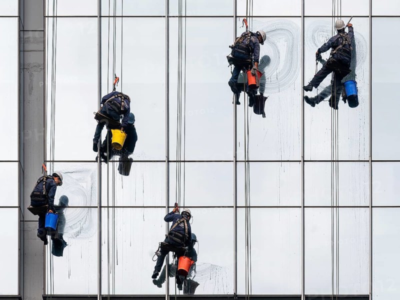 Employees of a cleaning company work vertically hanging on a rope while cleaning a glass façade on a high-rise building in Buenos Aires, Argentina