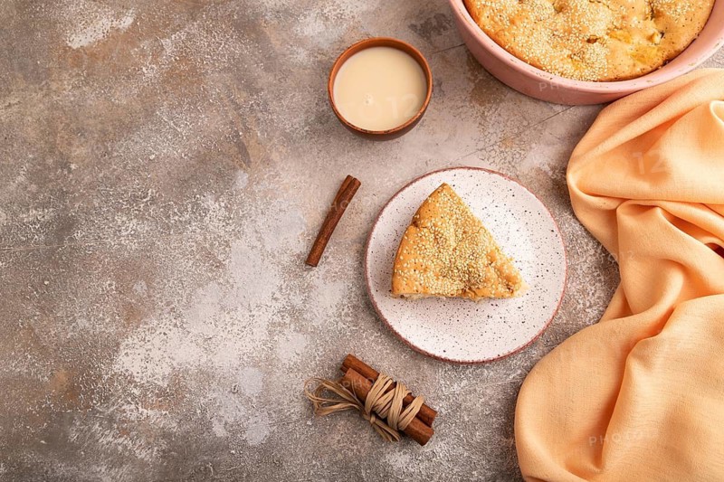 Apple Charlotte cake on brown concrete background and orange linen textile, cup of milk, top view, flat lay, copy space
