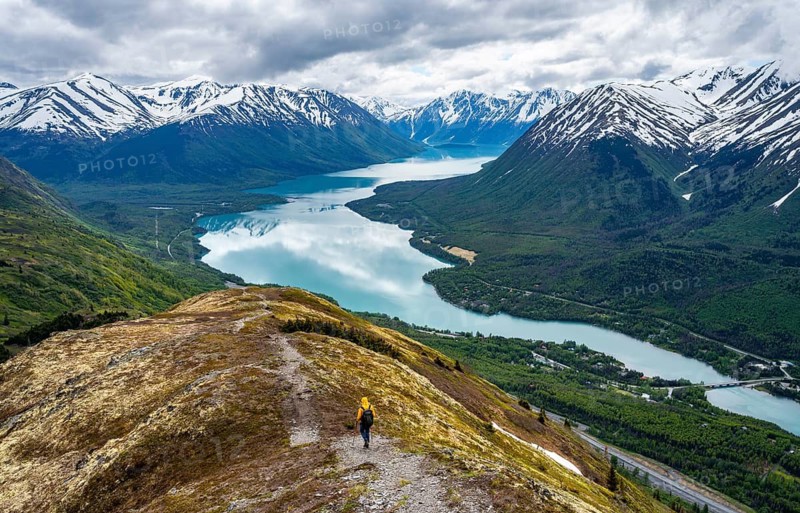 Climbers on a hiking trail on Slaughter Ridge, views of snowy mountains in spring and turquoise Lake Kenai Lake, Cooper Landing, Kenai Peninsula, Alaska, USA