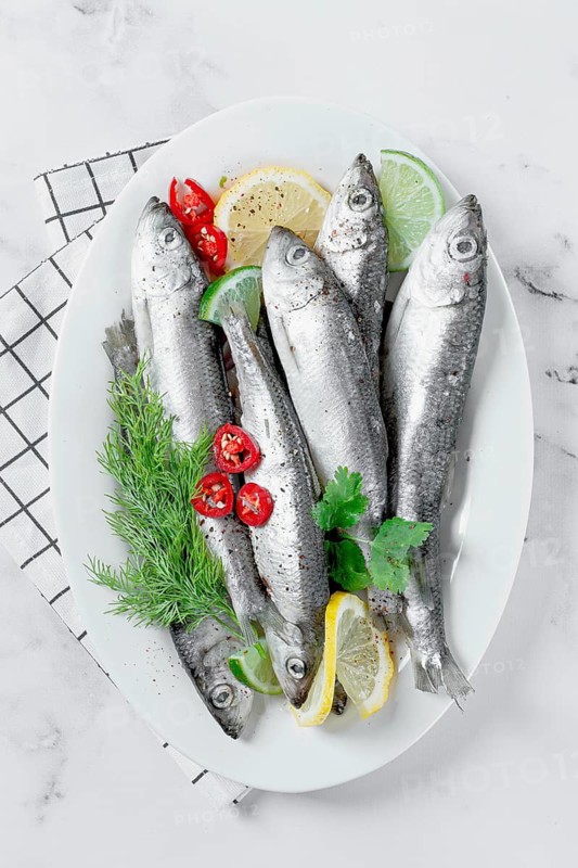 Fresh Herring fish, ready to cook, with herbs and spices, on a white platter, in the kitchen