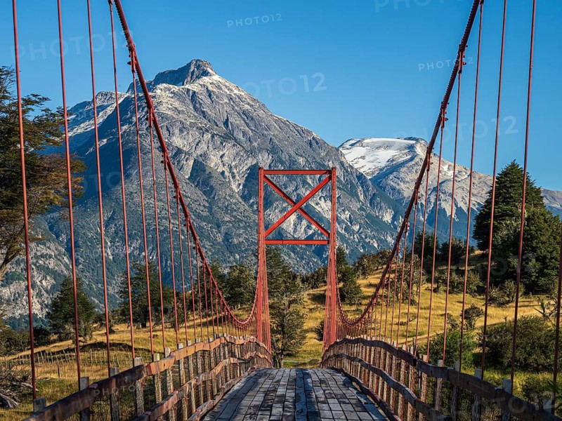 Old-style orange suspension bridge, river Rio Nadis south of Cochrane, mountain range at Rio Baker in the back, Patagonia, Chile