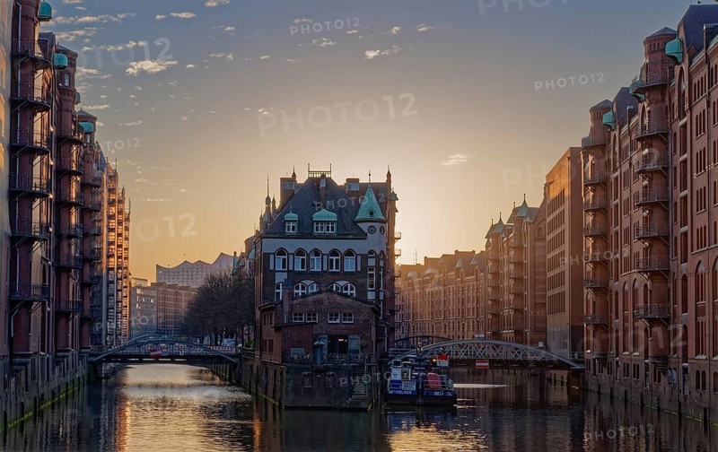 The moated castle in Hamburg's Speicherstadt between the Holländischbrookfleet and the Wandrahmfleet with the bridges of the Servant Row. At dusk, windows are illuminated. Speicherstadt, Hamburg, Germany