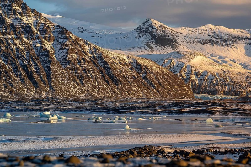 A stunning Icelandic winter scene captures the snow-capped peaks of Skaftafell scattered across a tranquil body of water, showcasing the raw beauty and serenity of nature