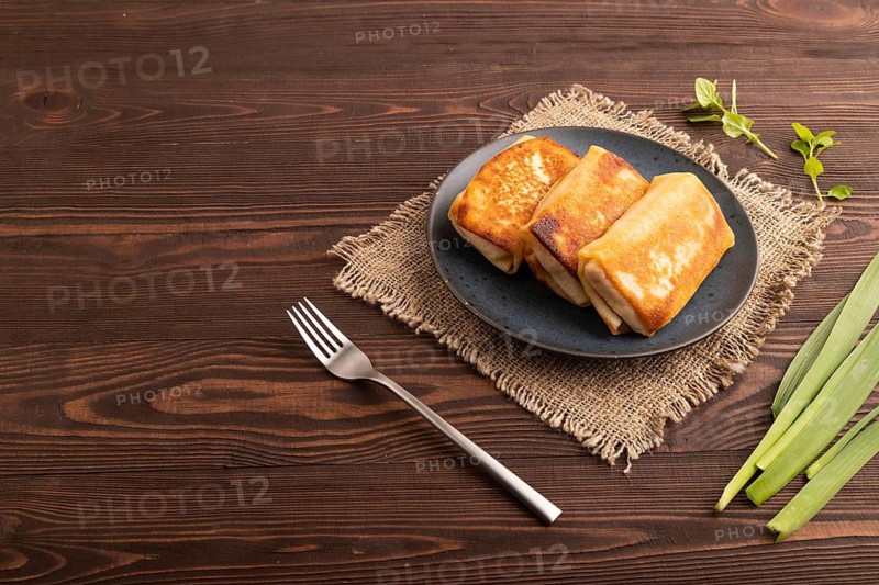 Fried crispy pancakes with meat and cheese on brown wooden background and linen textile. side view, copy space