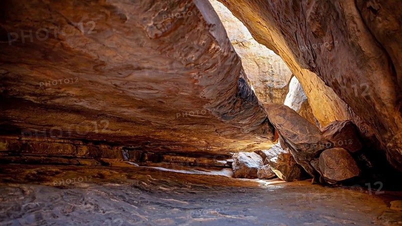 Entrance to a cave with penetrating sunlight and impressive rock formations, rocky landscape in the Sahara in Algeria