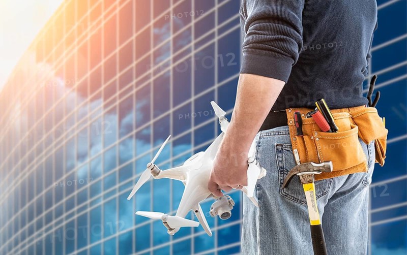 Construction Worker and Drone Pilot With Toolbelt Holding Drone At City High-Rise Building