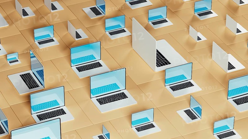 Numerous laptops arranged on a geometric backdrop illustrate the connection between technology and design. The vibrant displays enhance the aesthetic
