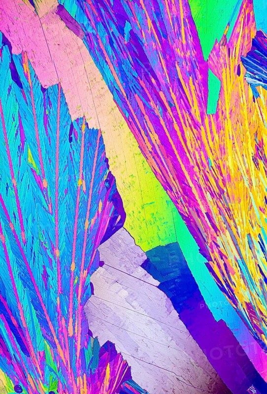 A dazzling microscopic image capturing the crystalline structure of Adipic acid, showcasing intense variations of blue, purple, yellow, green, and pink hues