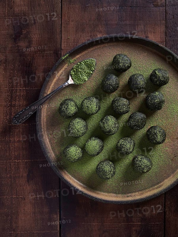 Matcha tea energy balls. Placed on a plate with a spoon full of matcha green tea powder. Healthy raw dessert, bliss balls or vegetarian truffles