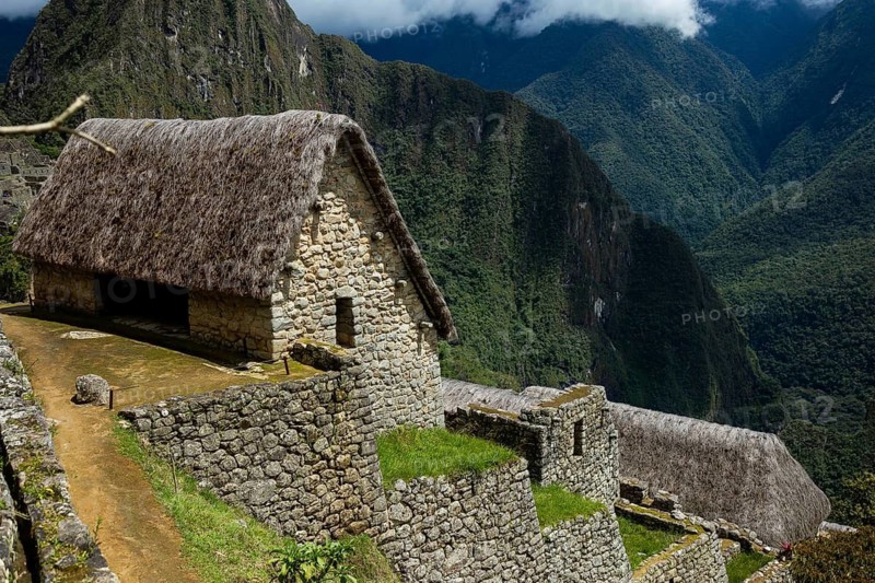 Breathtaking landscape of Machu Picchu in Peru, featuring an ancient Inca hut with a thatched roof surrounded by lush greenery and misty mountains