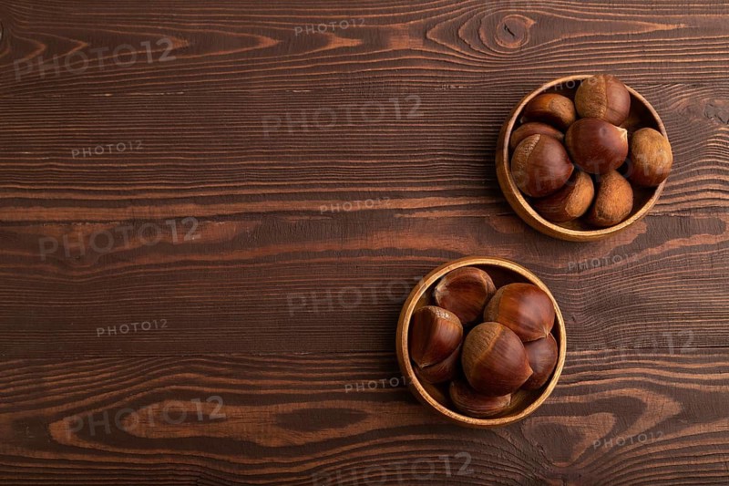 Wooden bowl with raw edible ?hestnuts on brown wooden background, top view, flat lay, copy space, minimalism