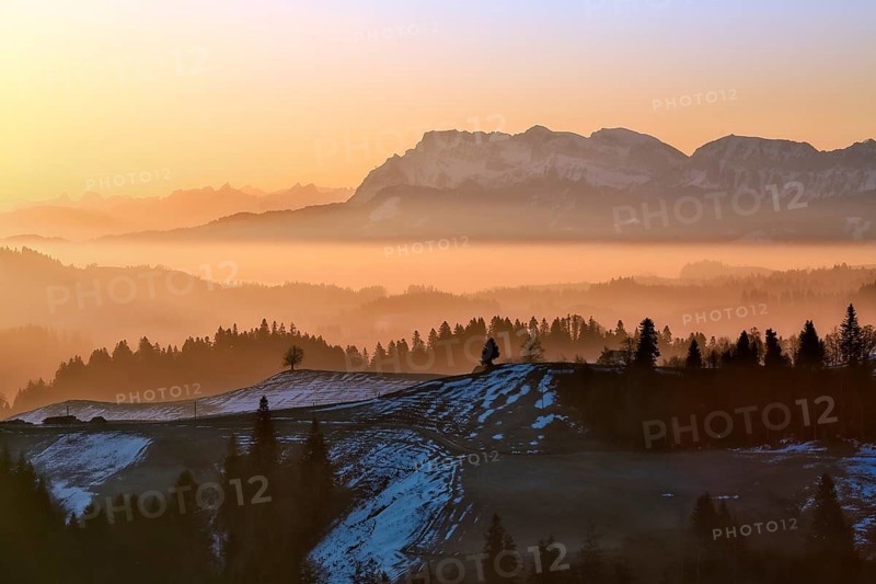 Misty morning atmosphere over hilly landscape with views of Mount Pilatus and Prealps, Entlebuch, Canton of Lucerne