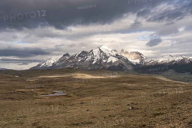 Snow-covered mountain range of the Paine massif with the Torres del Paine granite towers, wide steppe landscape with a small lake in the foreground under cloudy sky, Torres del Paine National Park, Patagonia, Chile