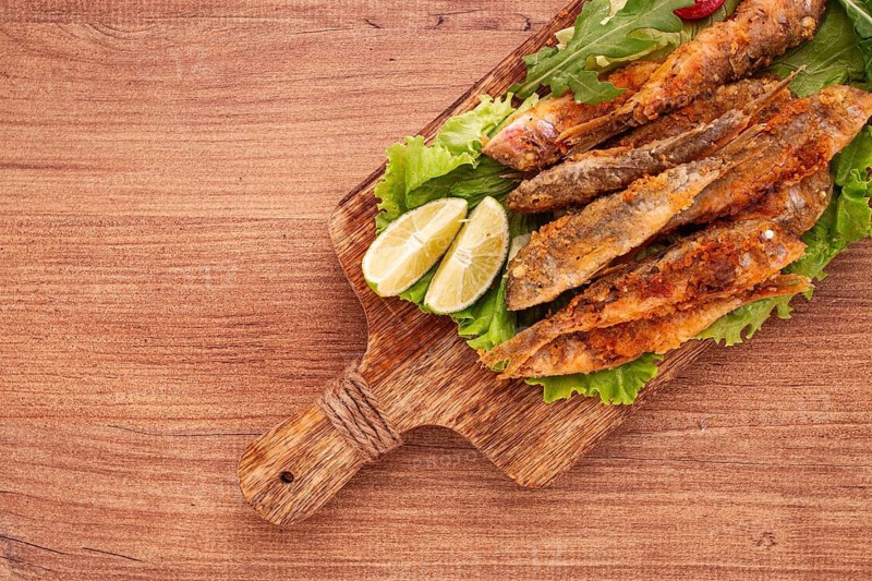 Fried crispy red mullet fish, on a wooden chopping board, with lime, no people