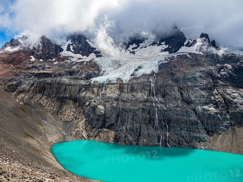 Lake below mountain Cerro Castillo, peak covered by clouds, glacier, glacial streams, nature reserve Cerro Castillo, Aysen, Chile