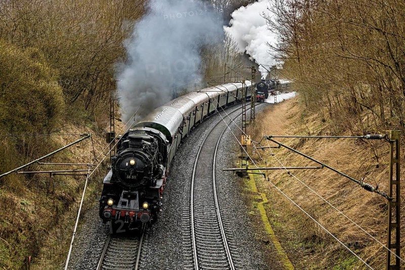 A steaming locomotive pulls a train through a winding wooded landscape, historic steam locomotive ride between Bebra and Sontra
