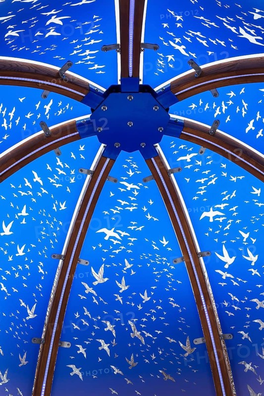 Close-up of backlit blue tinted plexiglass and curved wood panels canopy decorated with white flock of birds in flight theme motifs inside interactive cocoon rocking chair created by Olivier Landreville, Horizon Art Installation, Ile des Moulins, Old Terrebonne, Quebec, Canada