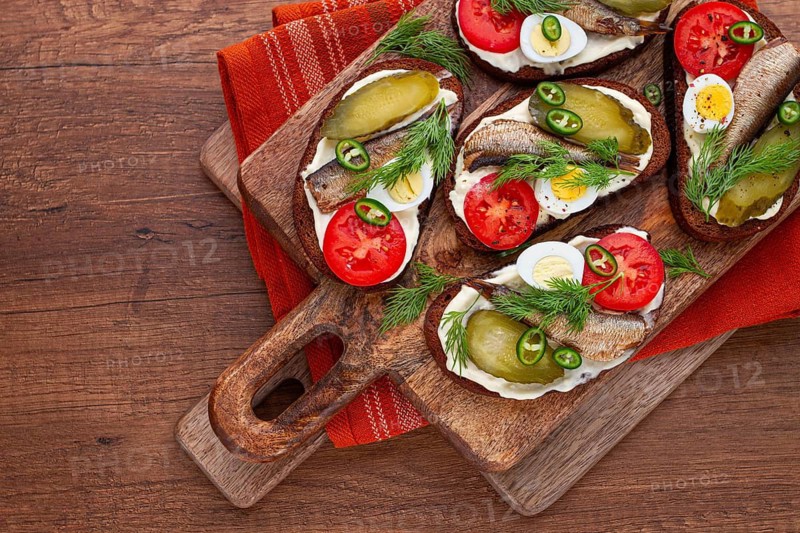 Sandwiches on rye bread with sprats, quail eggs, fresh tomatoes and pickled cucumber, on a wooden board, appetizer, breakfast