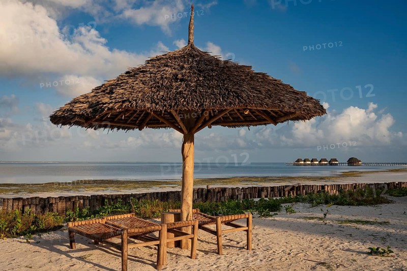 Traditional thatched beach umbrella and wooden sunbeds on a white sand beach with turquoise ocean and blue sky in a Zanzibar resort