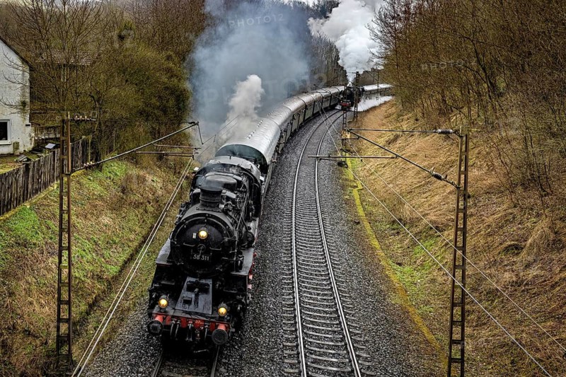 A black locomotive with steaming smoke follows winding tracks through nature, historic steam locomotive ride between Bebra and Sontra