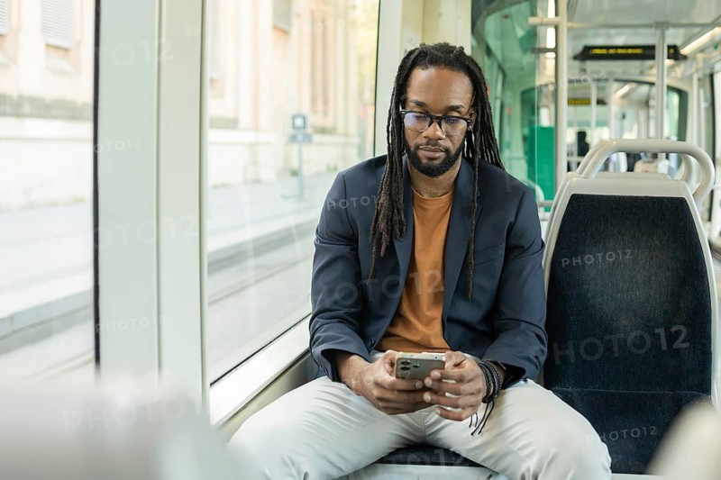 A cuban business man in a casual outfit uses his smartphone while seated on a modern, empty tram. The serene atmosphere and bright interior emphasize a moment of solitude