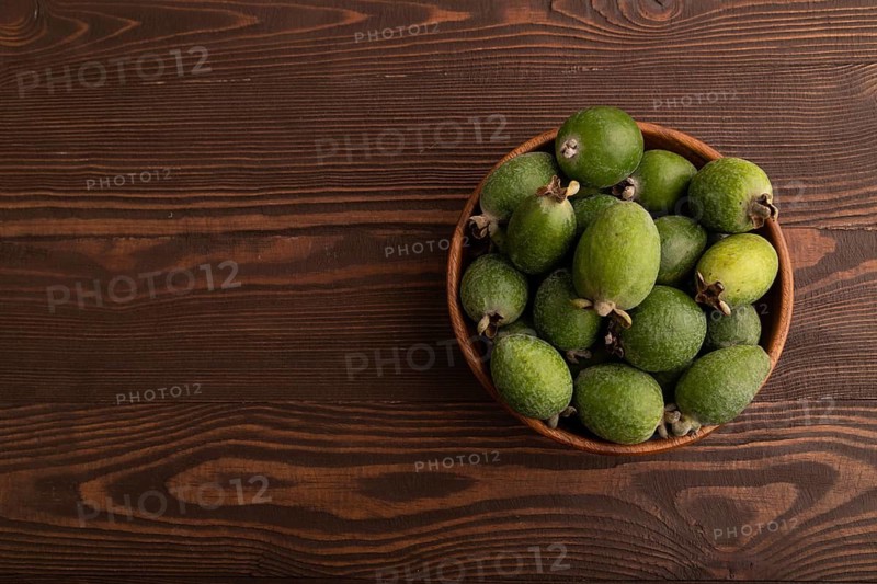 Ripe Feijoa in wooden bowl on brown wooden background, top view, flat lay, copy space, minimalism