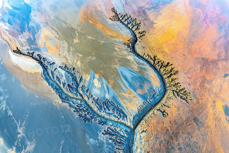 Aerial view of vibrant mud flats showcasing intricate fractal patterns with swirling textures and vivid colors. The natural artwork is an abstract masterpiece of earth's surface