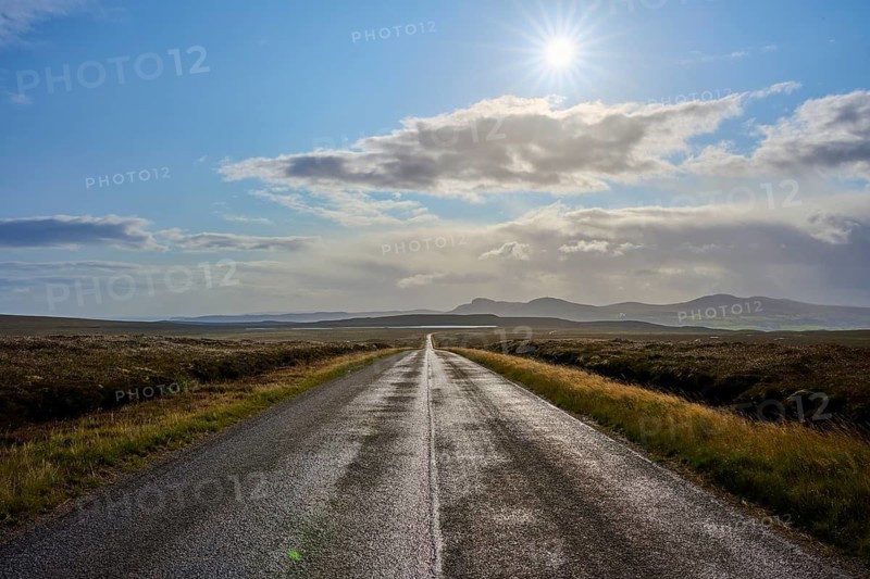 A sunlit road runs through a vast landscape with mountains in the background under a cloudy sky, Tongue, Lairg, Scotland, United Kingdom, Great Britain