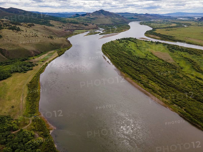 The Amur River flows gracefully through Vladivostok, surrounded by verdant hills and natural landscapes. This serene environment showcases the beauty of nature, with clear waters reflecting the sky above