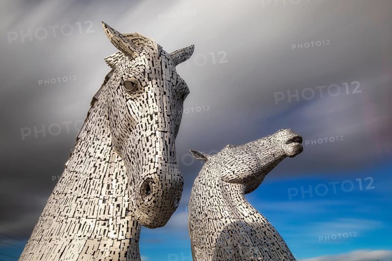 The Kelpies are two giant steel horse heads, each nearly 100 feet (30 metres) tall, located over the Forth & Clyde Canal in Falkirk, Scotland. They were designed by sculptor Andy Scott and completed in 2013 as a tribute to the horse-powered heritage of Scotland, celebrating the strength and endurance of the working horses that once powered the region's industry and canals. They are the largest pair of equine sculptures in the world
