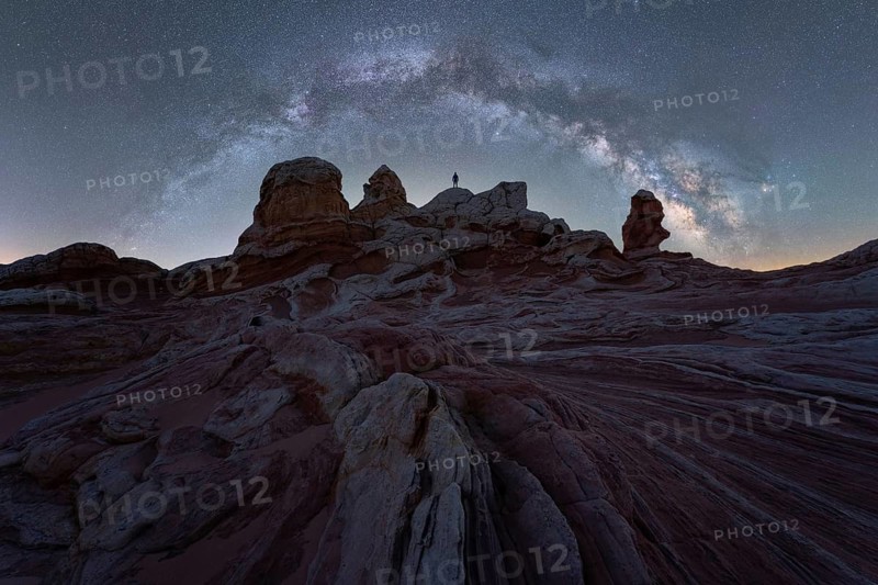 Unrecognizable person silhouetted against the Milky Way galaxy sprawling over the Utah desert's dramatic rock formations in a serene nighttime setting