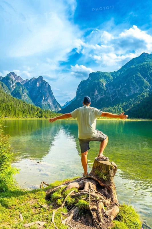 Tourist standing on a tree stump, embracing the stunning view of lake dobbiaco and the dolomites on a beautiful summer day