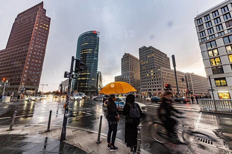 Potsdamer Platz Berlin in the evening with traffic on the streets. When it rains, the skyscrapers are reflected in puddles of water. People traveling with umbrellas. Berlin, Germany