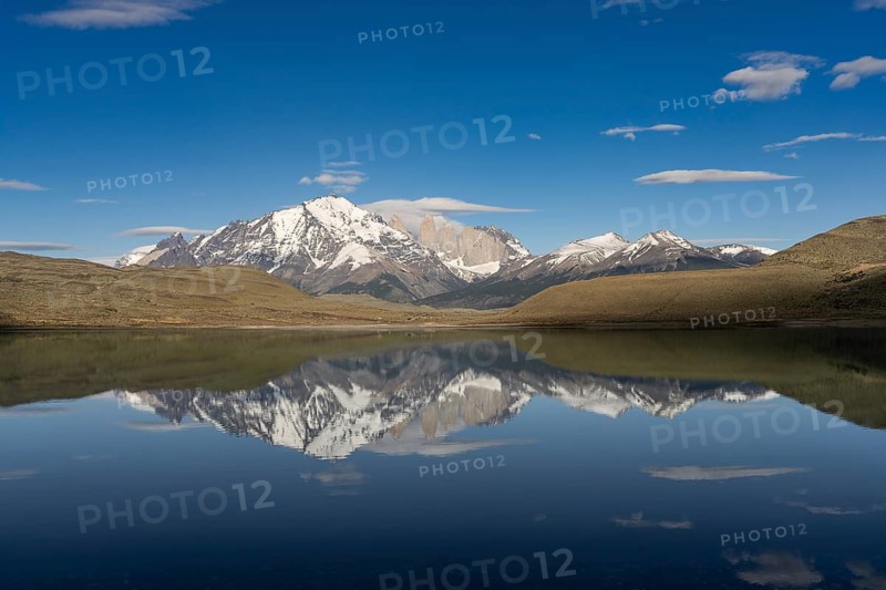 Granite towers of the Paine massif with snow-capped peaks are reflected in the Amarga lagoon, in front of it steppe landscape under blue sky, Torres del Paine National Park, Patagonia, Chile