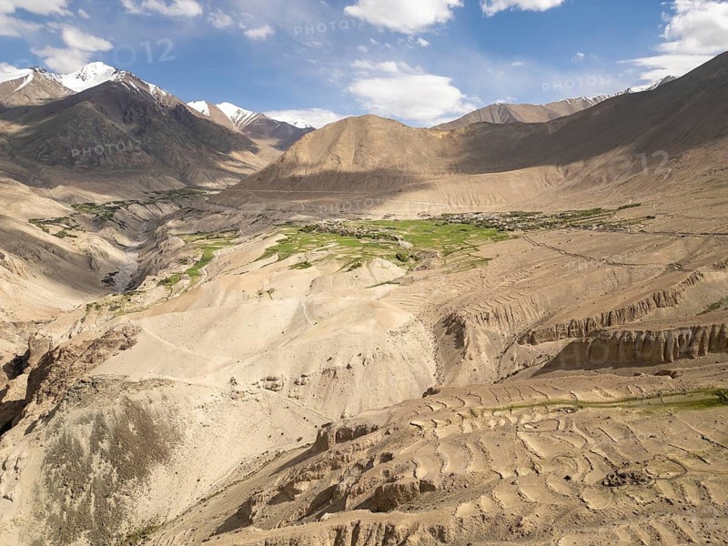 A breathtaking view of the arid landscape in Diskit, Nubra Valley, India, showcasing dramatic mountains, green patches of agriculture, and a bright sky above